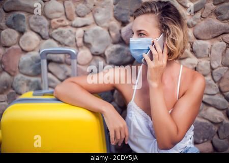 Frau mit Gepäck trägt medizinische Gesichtsmaske und mit Smartphone im Freien. Reise- und Coronavirus-Konzept Stockfoto