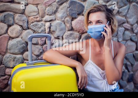 Frau mit Gepäck trägt medizinische Gesichtsmaske und mit Smartphone im Freien. Reise- und Coronavirus-Konzept Stockfoto