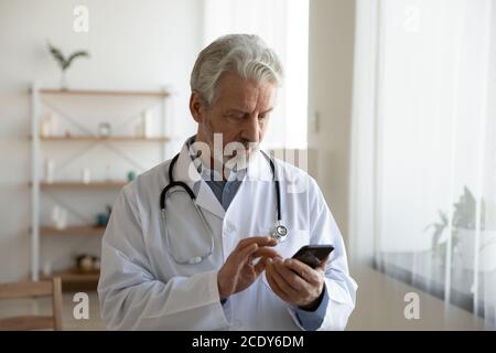 Ernst fokussierten reifen Arzt mit Telefon, Blick auf den Bildschirm Stockfoto