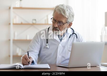 Serious reifen Arzt trägt eine Brille, die mit Dokumenten und Laptop arbeiten Stockfoto