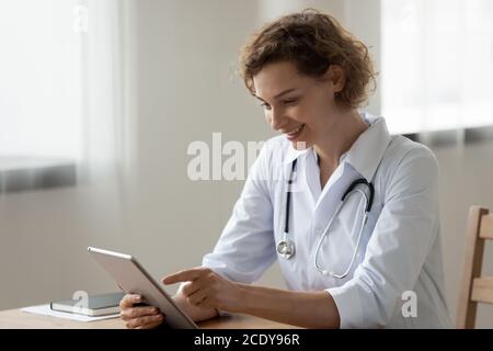Lächelnde junge Frau Arzt mit digitalen Tablet, sitzen am Schreibtisch Stockfoto