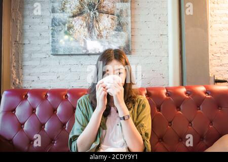 Schöne asiatische Frauen trinken heißen Kaffee sitzen auf vintage Sofa Im Café Stockfoto