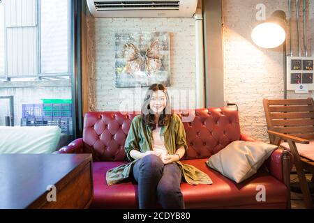 Schöne asiatische Frauen trinken heißen Kaffee sitzen auf vintage Sofa Im Café Stockfoto