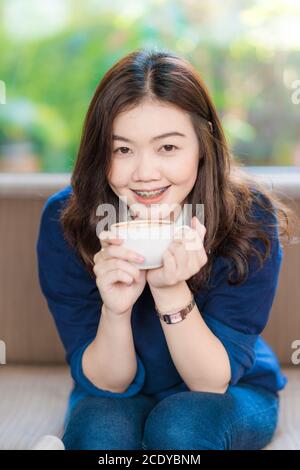 Schöne asiatische Frauen trinken heißen Kaffee sitzen auf vintage Sofa Im Café Stockfoto