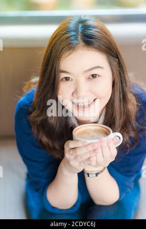 Schöne asiatische Frauen trinken heißen Kaffee sitzen auf vintage Sofa Im Café Stockfoto