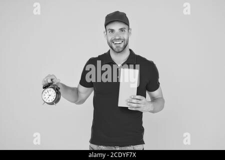 Echte Freude. Gehen Sie online einkaufen. Lieferung während der Quarantäne. Freundliche Mitarbeiter Mann. Lieferzeit. Lieferung Kurier mit Zeit Uhr Haltekasten. Nehmen Sie Ihr Paket. Geschenk Lieferung Mann mit Vintage Uhr. Stockfoto