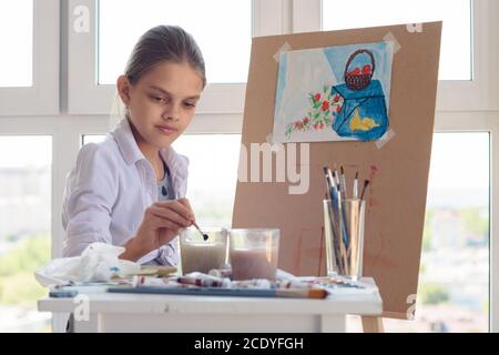 Mädchen sitzt hinter einer Staffelei und wäscht ihre Bürste in einem Glas Wasser Stockfoto