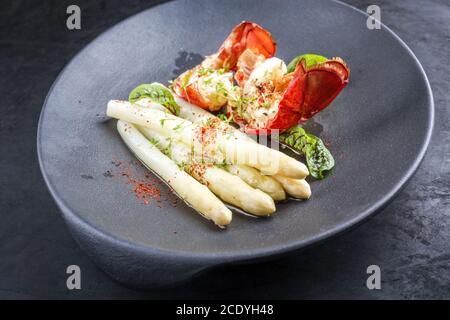 Traditionelle Grill stacheligen Hummerschwanz geschnitten und mit Weiß angeboten Spargel und Salat als Nahaufnahme auf einem Teller mit modernem Design Stockfoto