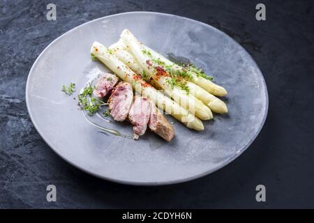 Gebratenes iberisches Schweinefilet in Scheiben geschnitten mit blanchierten weißen Spargel und Kräuter mit Gewürzen als Nahaufnahme auf einem modernen Design-Teller Stockfoto