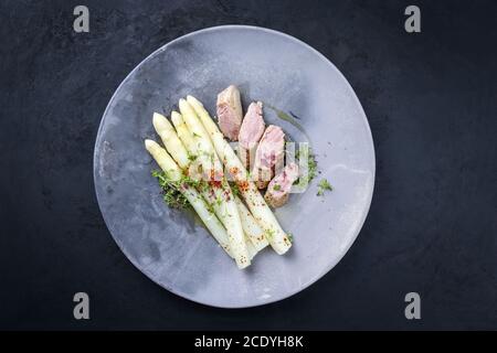 Gebratenes iberisches Schweinefilet in Scheiben geschnitten mit blanchierten weißen Spargel und Kräuter mit Gewürzen als Nahaufnahme auf einem modernen Design-Teller Stockfoto