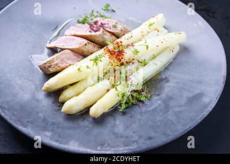 Gebratenes iberisches Schweinefilet in Scheiben geschnitten mit blanchierten weißen Spargel und Kräuter mit Gewürzen als Nahaufnahme auf einem modernen Design-Teller Stockfoto