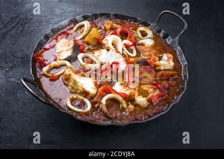 Traditioneller brasilianischer Fischeintopf Moqueca capixaba mit Fischfilet und Tintenfisch Ringe in Tomatensauce als Nahaufnahme in einem rustikalen Schwenken Stockfoto