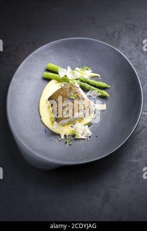 Traditionelles frittiertes Kabeljau-Fischfilet mit grünen Spargelspitzen Und Kartoffelpüree in Parmesan-Olivenöl-Sauce als Nahaufnahme Stockfoto