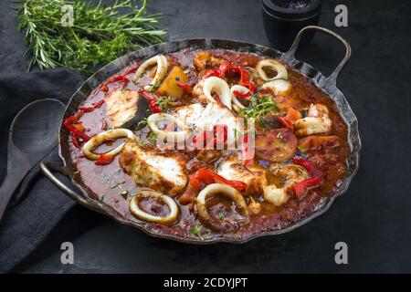Traditioneller brasilianischer Fischeintopf Moqueca capixaba mit Fischfilet und Tintenfisch Ringe in Tomatensauce als Nahaufnahme in einem rustikalen Schwenken Stockfoto