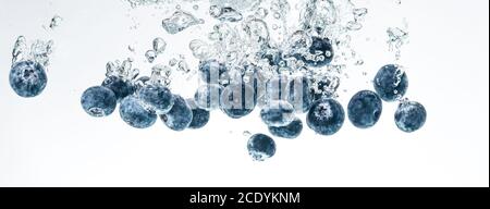 Blaubeeren sinken in Wasser mit Luftblasen auf weißem Hintergrund. Stockfoto