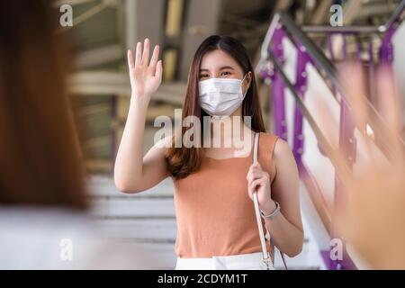 Junge asiatische Frau Passagier trägt chirurgische Maske und winkende Hand für die Begrüßung ihrer Freundin in U-Bahn-Zug, wenn Sie in der großen Stadt in Covid19 out Stockfoto