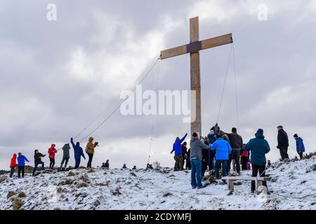 Menschen (Christen) verwenden Seile, um ein riesiges schweres hölzernes Osterkreuz (Faith Symbol) auf einem verschneiten Hügel zu heben - der Chevin, Otley, Yorkshire, Großbritannien. Stockfoto