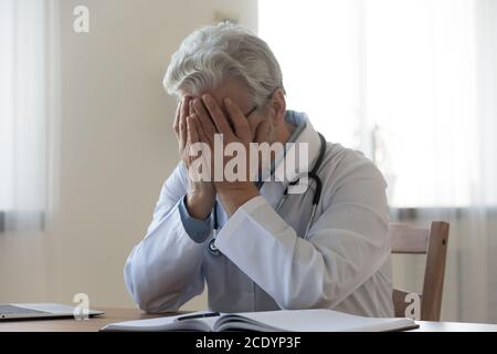Gestresst frustriert reifer Arzt, der Gesicht mit Händen bedeckt Stockfoto