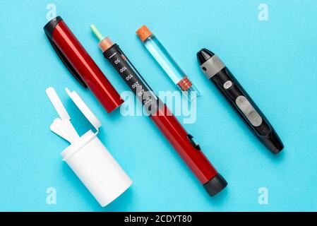 Diabetesset Lanzette mit Ersatznadeln, Streifen, Schachtel mit Ersatzstreifen, Stiftinjektor, Ersatzinsulin und Stiftnadeln auf blauem Hintergrund. Stockfoto