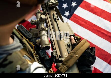 Nahaufnahme eines amerikanischen Soldaten, der sein Gewehr über der Nationalflagge hält Während der Vorbereitung auf den Kampf Stockfoto