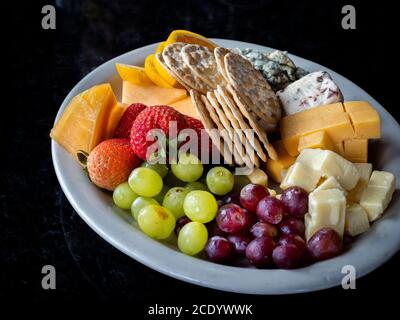 Obstkäse und Cracker und ein Teller auf einem schwarzen Hintergrund Stockfoto