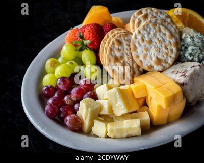 Obstkäse und Cracker und ein Teller auf einem schwarzen Hintergrund Stockfoto