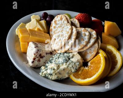 Obstkäse und Cracker und ein Teller auf einem schwarzen Hintergrund Stockfoto