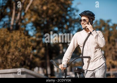 Sichere Fahrradtour. Lächelnder Kerl im Helm spricht per Smartphone Stockfoto