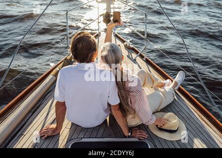 Rückansicht des älteren Mannes und der Frau, die privat sitzen yacht und Selfie mit Handy Stockfoto