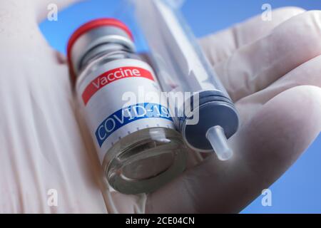 Nahaufnahme von Handschuhen mit Coronavirus-Impffläschchen und Spritze Stockfoto