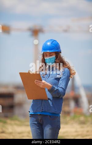 Junge Frau Ingenieur trägt Gesichtsmaske und hält Zwischenablage mit Dokumente Stockfoto