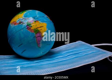 Medizinische Schutzmaske auf schwarzem Hintergrund mit kleiner Welt. Chirurgische Gesichtsmaske. Coronavirus - covid-19 Stockfoto