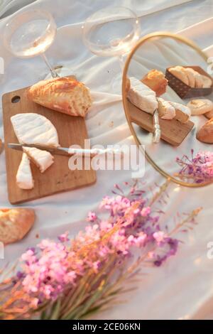 Sommer - Picknick. Käse Brie, Baguette, Pfirsiche, Champagner, Spiegelei, Blumen und Korb Stockfoto