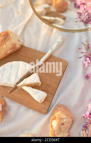 Sommer - Picknick. Käse Brie, Baguette, Pfirsiche, Champagner, Spiegelei, Blumen und Korb Stockfoto