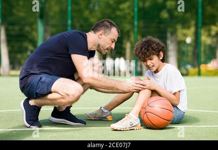 Lehrer hilft Jungen mit Knie Trauma nach dem Basketball spielen Stockfoto