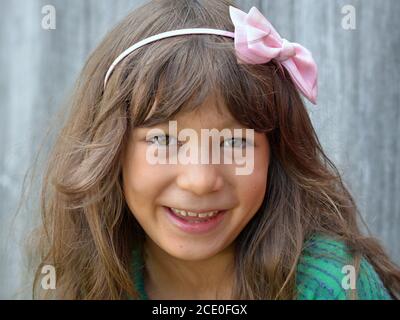 Niedliche kleine gemischte Rasse Tween Mädchen (kaukasischen und ostasiatischen) mit rosa Schleife Knoten Stirnband lächelt für die Kamera. Stockfoto