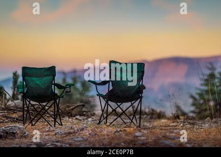 Zwei leere Campingstühle stehen auf dem Gipfel des Berges. Der perfekte Ort, um den Sonnenuntergang zu beobachten. Aktive Entspannung Lifestyle Stockfoto