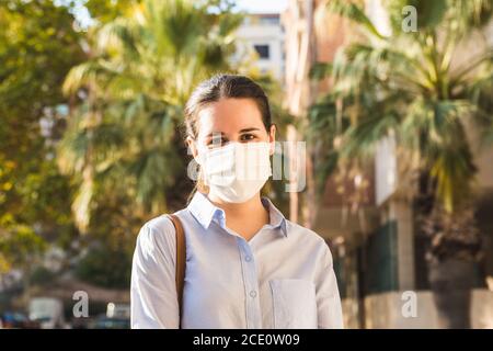 Stock Foto von einer jungen Frau trägt eine Gesichtsmaske Blick auf die Kamera auf der Straße an einem sonnigen Tag Stockfoto