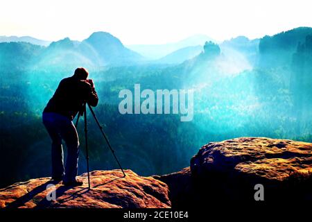 Filmkörnung. Professionell auf der Klippe. Naturfotograf macht Fotos mit Spiegelkamera auf dem Berg Stockfoto