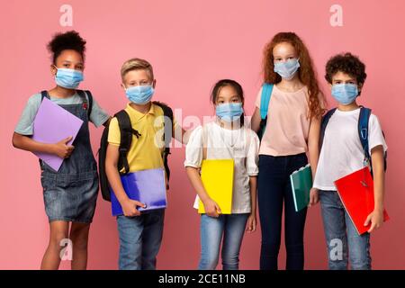 Ausbildung während Quarantäne. Porträt von verschiedenen Schulkindern in medizinischen Masken auf rosa Hintergrund Stockfoto