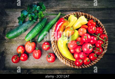 Ernte des frischen reifen Gemüses auf Holztisch und in Stabschüssel - Pfeffer, Tomate, Gurke, Sellerie Blätter. Gesunde Bio-Lebensmittel, Sommer-Vitamine, Bio Stockfoto
