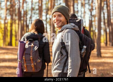 Lächelnder junger Backpacker beim Wandern mit Freunden im Wald Stockfoto