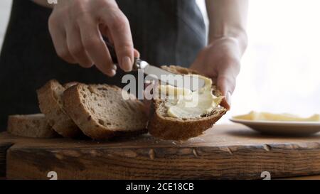 Butter auf Brot verteilen. Frauenhände machen Sandwich mit Brot und Butter Stockfoto