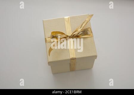 Überraschung mit anwesenden Konzept. Beige geschlossene Geschenkbox Verpackung mit glänzenden Gold Farbband isoliert auf grauem Hintergrund. Oben, Nahaufnahme, hoher Winkel V Stockfoto