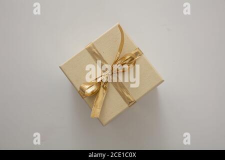 Überraschung mit anwesenden Konzept. Beige geschlossene Geschenkbox Verpackung mit glänzenden Gold Farbband isoliert auf grauem Hintergrund. Draufsicht. Stockfoto