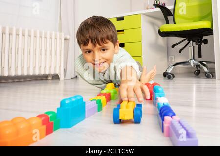 Kleiner glücklicher Junge spielt mit Spielzeug, das auf dem Boden liegt Und das Auto schieben Stockfoto