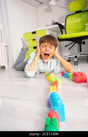 Autistischer Junge legte Spielzeug in einer Reihe lag auf der Boden schreien und Ohren mit Händen bedecken Stockfoto