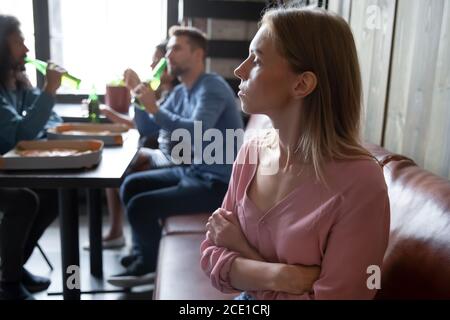 Verärgert junge Frau sitzt abgesehen von verschiedenen Freunden im Café Stockfoto