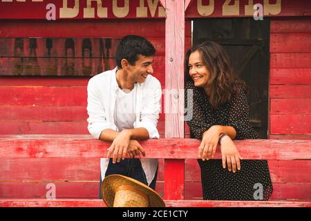 Hübsches Paar Flirten und lächeln sich gegenseitig außerhalb eines roten Holzsalons. Ranch Konzept Fotografie Stockfoto