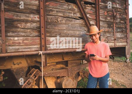 Junger Mann mit Jeans und einem Cowboy Hut mit seinem Smartphone mit Freunden zu kommunizieren. Ranch Konzept Fotografie Stockfoto